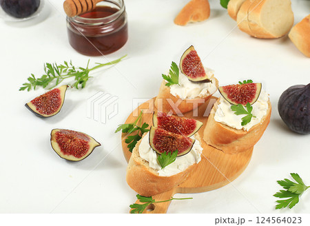 Healthy breakfast with ingredients, toast with figs and soft cream cheese and honey, Canape or crostini with fried baguette and herbs on a light sunny table, italian recipes menu, selective focus 124564023