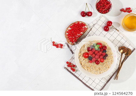 Healthy breakfast with ingredients, oatmeal pudding or porridge with raspberries, cherries, currants, honey and toast on a sunny table. The concept of healthy and natural food, lifestyle, food for Healthy breakfast with ingredients, oatmeal pudding or porridge with raspberries, cherries, currants, honey and toast on a sunny table. The concept of healthy and natural food, lifestyle, food for 124564270