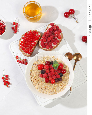 Healthy breakfast with ingredients, oatmeal pudding or porridge with raspberries, cherries, currants, honey and toast on a sunny table. The concept of healthy and natural food, lifestyle, food for Healthy breakfast with ingredients, oatmeal pudding or porridge with raspberries, cherries, currants, honey and toast on a sunny table. The concept of healthy and natural food, lifestyle, food for 124564271