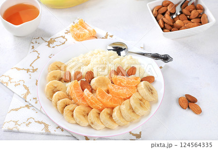 Useful breakfast with ingredients, flat lay, rice pudding with bananas, honey, tangerines and almonds on a sunny table. Healthy and natural food concept, lifestyle, food for children, selective focus 124564335