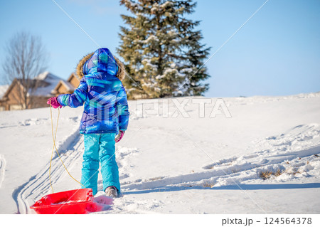 Girl in winter clothing walking a sled up a snow covered hill. Girl in winter clothing walking a sled up a snow covered hill. 124564378