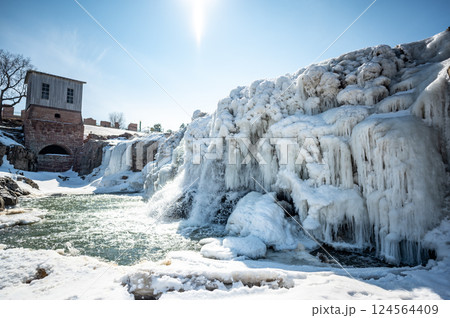 Sioux Falls Park waterfall with ice and snow. Cascading snowmelt water pouring over the top into a pool of standing water. Sioux Falls Park waterfall with ice and snow. Cascading snowmelt water pouring over the top into a pool of standing water. 124564409