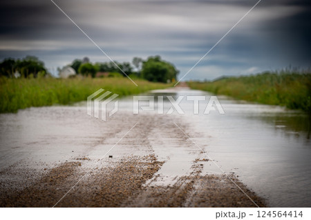 Selective focus on the gravel leading into floodwater covering the road in a rural area 124564414