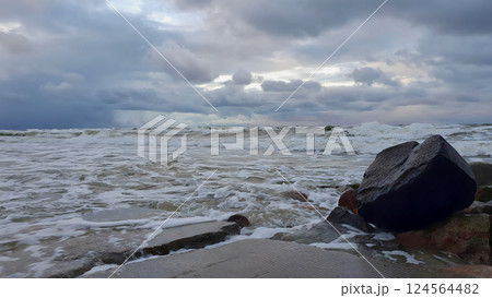 Scenic seaside landscape on Baltic sea coast with stormy waves roll over stone pier slabs on empty rocky shore under dramatic sky with storm clouds at winter dusk. No people desolate seascape. 124564482