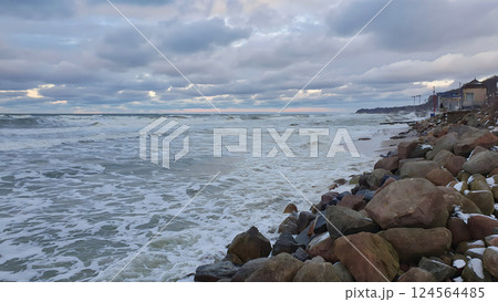 Scenic seaside landscape of severe Baltic sea coast with stormy waves rolling on boulders on empty rocky shore under dramatic sky with storm clouds at winter dusk. No people desolate seascape. 124564485