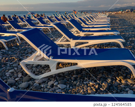 Beach chairs. Lots of empty sunbeds on the pebbles. The concept of commerce on the beach. Sunbed rental at the resort. At sunset. Rest of people on the sea. Beach chairs. Lots of empty sunbeds on the pebbles. The concept of commerce on the beach. Sunbed rental at the resort. At sunset. Rest of people on the sea. 124564585
