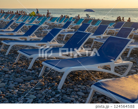 Beach chairs. Lots of empty sunbeds on the pebbles. The concept of commerce on the beach. Sunbed rental at the resort. At sunset. Rest of people on the sea. Beach chairs. Lots of empty sunbeds on the pebbles. The concept of commerce on the beach. Sunbed rental at the resort. At sunset. Rest of people on the sea. 124564588