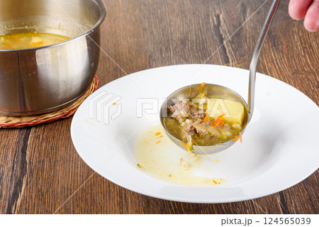 Ladle Leningrad Rassolnik soup into a plate. 124565039