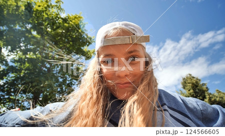 Cheerful schoolgirl in cap, wind tousling hair, basking in bright sunlight while playing outdoors in park setting Cheerful schoolgirl in cap, wind tousling hair, basking in bright sunlight while playing outdoors in park setting 124566605