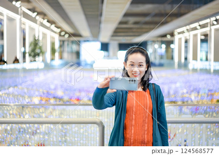 Asian Woman in green orange cloth selfies in shopping mall which is a colorful light place. Asian Woman in green orange cloth selfies in shopping mall which is a colorful light place. 124568577