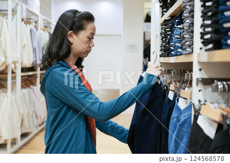 Backside of a Woman wearing without face mask was selecting navy pants on a shelf in clothes shop at department stores. Backside of a Woman wearing without face mask was selecting navy pants on a shelf in clothes shop at department stores. 124568578
