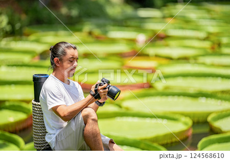 Asian Man is holding a camera and taking a photo at outdoor field with the Lily Lotus Leaf pond background. 124568610