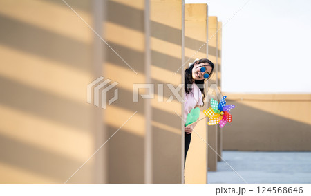 Asian woman posts and play Windmill Toy colourful rainbow colour on the building rooftop in sunset time. Asian woman posts and play Windmill Toy colourful rainbow colour on the building rooftop in sunset time. 124568646