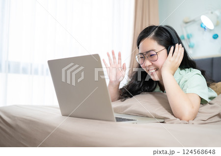 Beautiful Asian woman using zoom meeting and making facetime video, social distancing during covid pandemic period on her bedroom with a pastel green - brown color theme. Beautiful Asian woman using zoom meeting and making facetime video, social distancing during covid pandemic period on her bedroom with a pastel green - brown color theme. 124568648