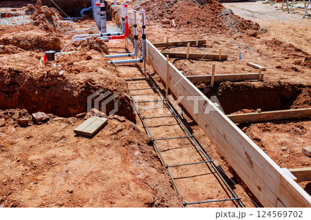 Foundation preparation is in progress at construction site with wooden forms, wastewater plumbing pipe installations visible. Foundation preparation is in progress at construction site with wooden forms, wastewater plumbing pipe installations visible. 124569702