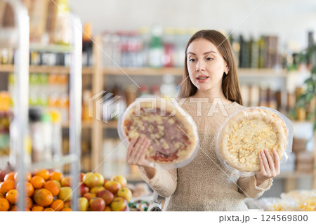 Female buyer carefully reads labels on frozen pizza - she chooses the best product in supermarket 124569800