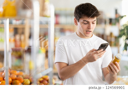 Young man customer at shop scans QR code on smoothie package using phone camera Young man customer at shop scans QR code on smoothie package using phone camera 124569901