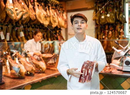 Cheerful young butcher shop salesman holding leg of Iberian ham 124570087