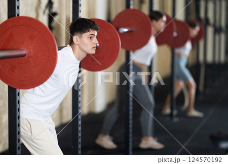 Young guy training with barbell in gym Young guy training with barbell in gym 124570192