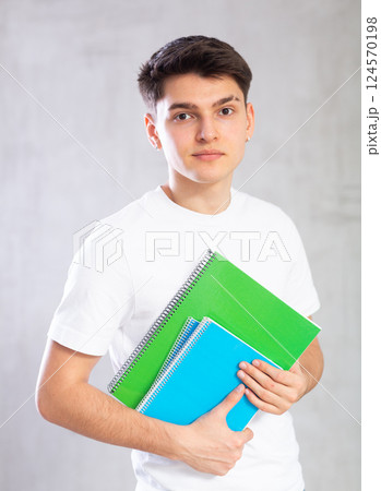 Smiling young student posing with workbooks against gray shadeless background Smiling young student posing with workbooks against gray shadeless background 124570198