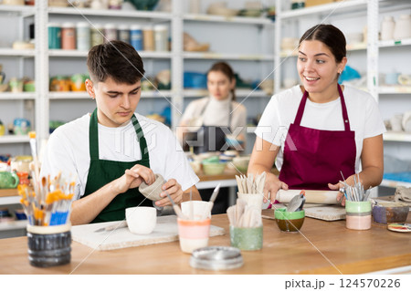 Joyous young man and woman sculpting handmade cups 124570226