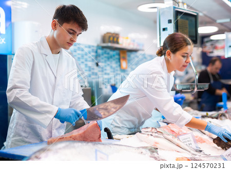 Seller with knife cut fish in supermarket near counter 124570231