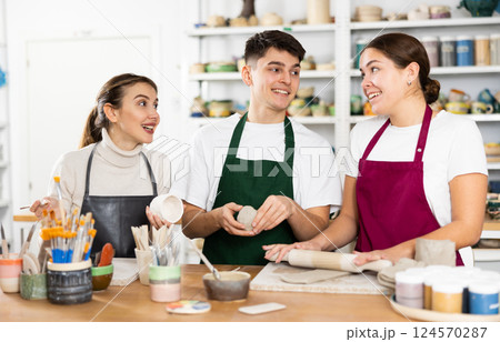 Joyous young man and women sculpting handmade cups 124570287