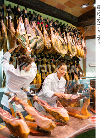 Young couple work together in butcher shop - they cut traditional Spanish jamon 124570288