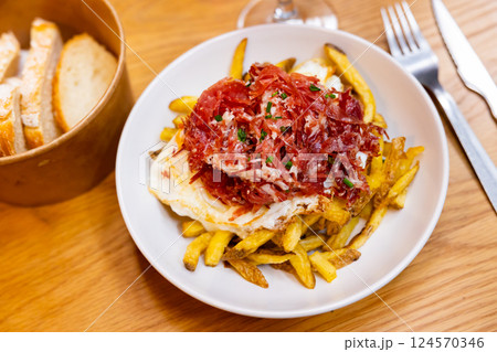 Fried eggs cooked spanish style with potatoes and slices of hamon with sliced bread glass of wine and cutlery Fried eggs cooked spanish style with potatoes and slices of hamon with sliced bread glass of wine and cutlery 124570346