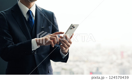 オフィスで都市を背景にスマホを使う男性ビジネスパーソン オフィスで都市を背景にスマホを使う男性ビジネスパーソン 124570439