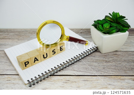 Magnifying glass with wooden blocks alphabet letters PAUSE text message on wooden background 124571635