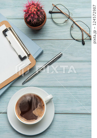 Office desk with coffee, clipboard, eyeglasses and cactus on wooden background 124572987