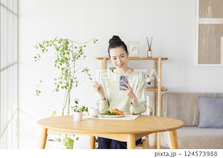 スマホを見ながら食事をとる女性 スマホを見ながら食事をとる女性 124573988
