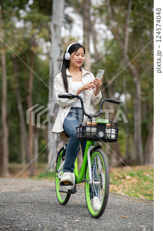 A woman looking happily at her notebook as she figure something out while sitting on park sidewalk 124574048