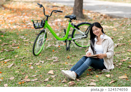 A woman looking happily at her notebook as she figure something out while sitting on park sidewalk 124574050