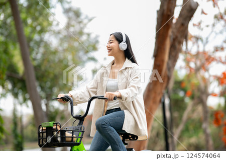 A woman looking happily at her notebook as she figure something out while sitting on park sidewalk 124574064
