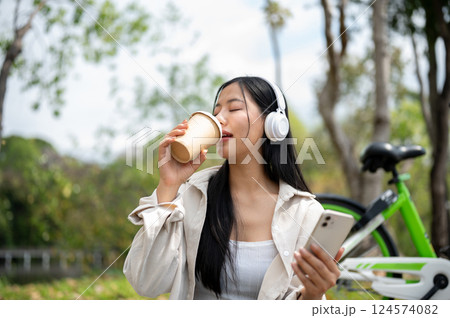 A woman looking happily at her notebook as she figure something out while sitting on park sidewalk 124574082