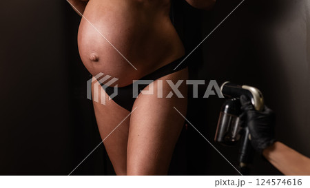 Faceless pregnant woman getting an instant tan. The master applies bronzer with a spray. Faceless pregnant woman getting an instant tan. The master applies bronzer with a spray. 124574616