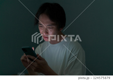 暗い部屋の中でスマホを操作する男性 124575879