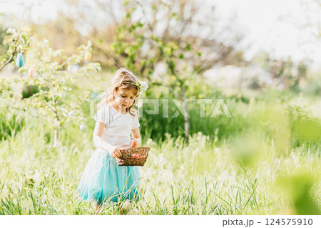 Easter egg hunt. Girl child Wearing Bunny Ears Running To Pick Up Egg In Garden. Easter tradition. Baby with basket full of colorful eggs. Easter egg hunt. Girl child Wearing Bunny Ears Running To Pick Up Egg In Garden. Easter tradition. Baby with basket full of colorful eggs. 124575910