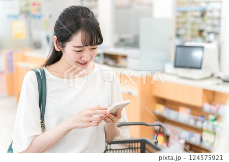 薬局・ドラッグストア・コンビニエンスストアでスマホを見ながら化粧品・コスメの買い物をする女性 124575921