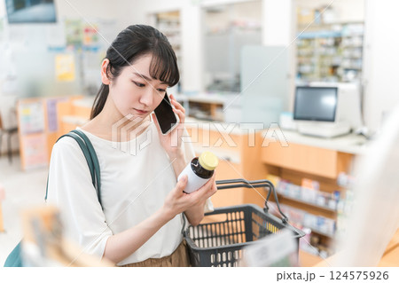 薬局・ドラッグストアで電話・通話しながら買い物をする困る・悩むアジア人女性 124575926