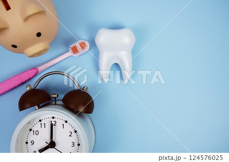 White tooth model with toothbrus, alarm clock and piggy bank on blue background, dental hygiene concept 124576025