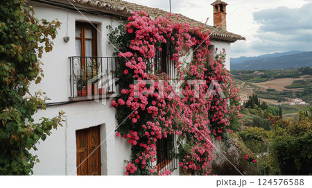 white Spanish countryside house with rustic wooden doors and windows, beautifully adorned with cascading pink roses 124576588