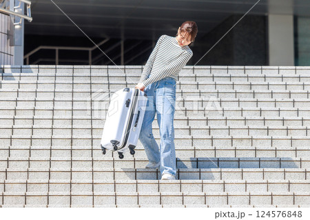 重いスーツケースを持って階段を降りる女性 124576848