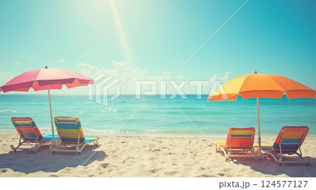 Colorful beach umbrellas and lounge chairs on sandy shore facing turquoise ocean under blue sky. Summer vacation and travel concept 124577127