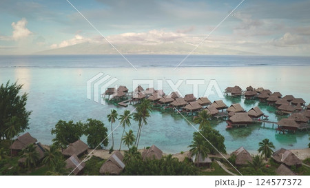 Breathtaking aerial view overwater bungalows in crystal clear turquoise water of French Polynesia, green vegetation and a distant island palm trees. Exotic travel vacation getaway, romantic honeymoon Breathtaking aerial view overwater bungalows in crystal clear turquoise water of French Polynesia, green vegetation and a distant island palm trees. Exotic travel vacation getaway, romantic honeymoon 124577372