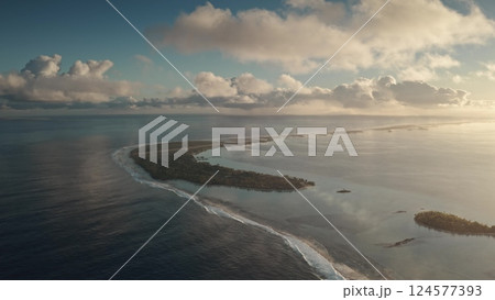 An aerial perspective captures a stunning coastal landscape where clear blue waters meet a lush green island. Gentle waves lap against the shore under a dramatic sky filled with clouds during sunset. An aerial perspective captures a stunning coastal landscape where clear blue waters meet a lush green island. Gentle waves lap against the shore under a dramatic sky filled with clouds during sunset. 124577393