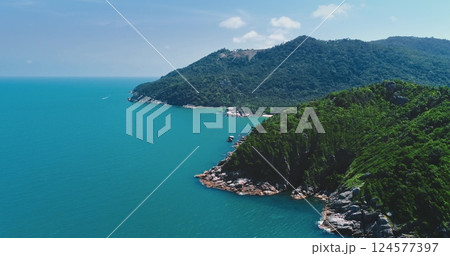 Turquoise waters gently caressing rocky shores of a lush tropical island, with a small boat navigating the tranquil sea and a verdant mountain as a stunning backdrop Turquoise waters gently caressing rocky shores of a lush tropical island, with a small boat navigating the tranquil sea and a verdant mountain as a stunning backdrop 124577397