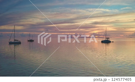 Stunning sunset sky reflecting on the calm ocean with sailboats anchored near Bora Bora island in French Polynesia, creating a tranquil and picturesque scene 124577405